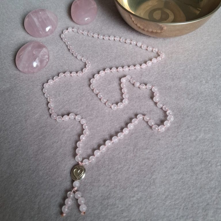 Perlenkette aus Rosenquarz, umgeben von Kristallen und einer Klangschale.