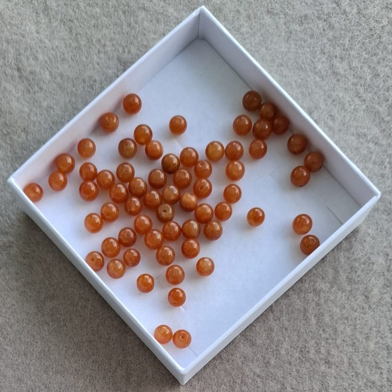 organge Aventurin Perlen Eine kleine Schachtel mit orangefarbenen Perlen auf einem hellen Untergrund.