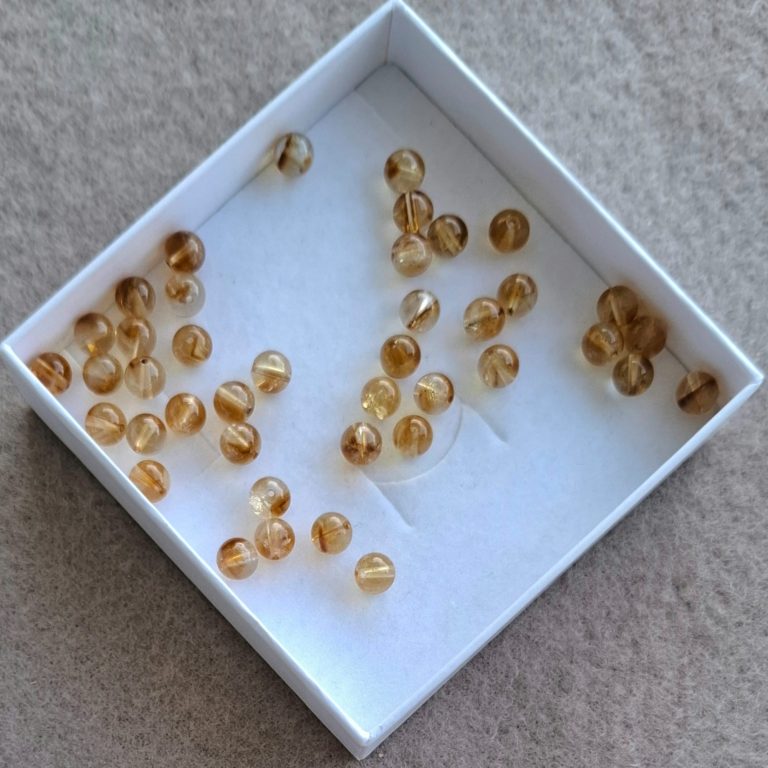 Citrin Perlen Eine kleine Schachtel mit vielen transparenten, gelben Perlen.