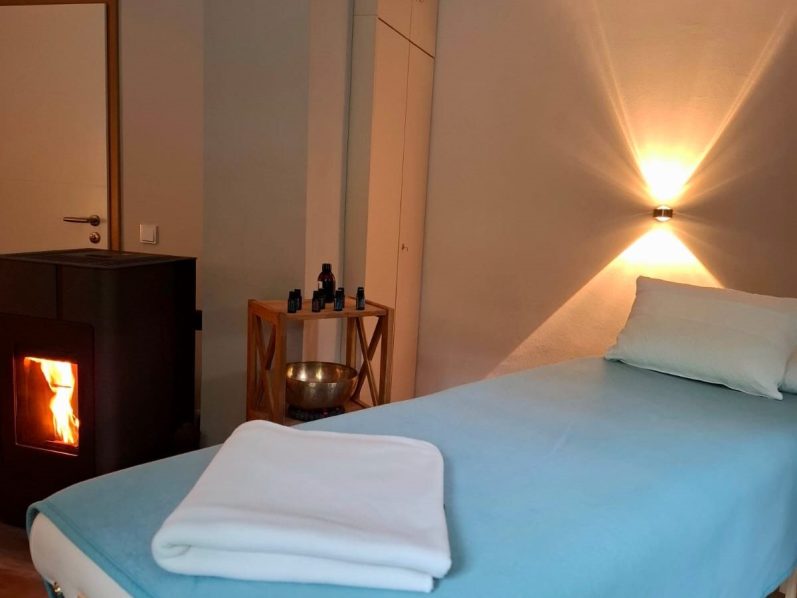 Ein gemütlicher Raum mit Massagetisch, Schalen und einem Kamin.