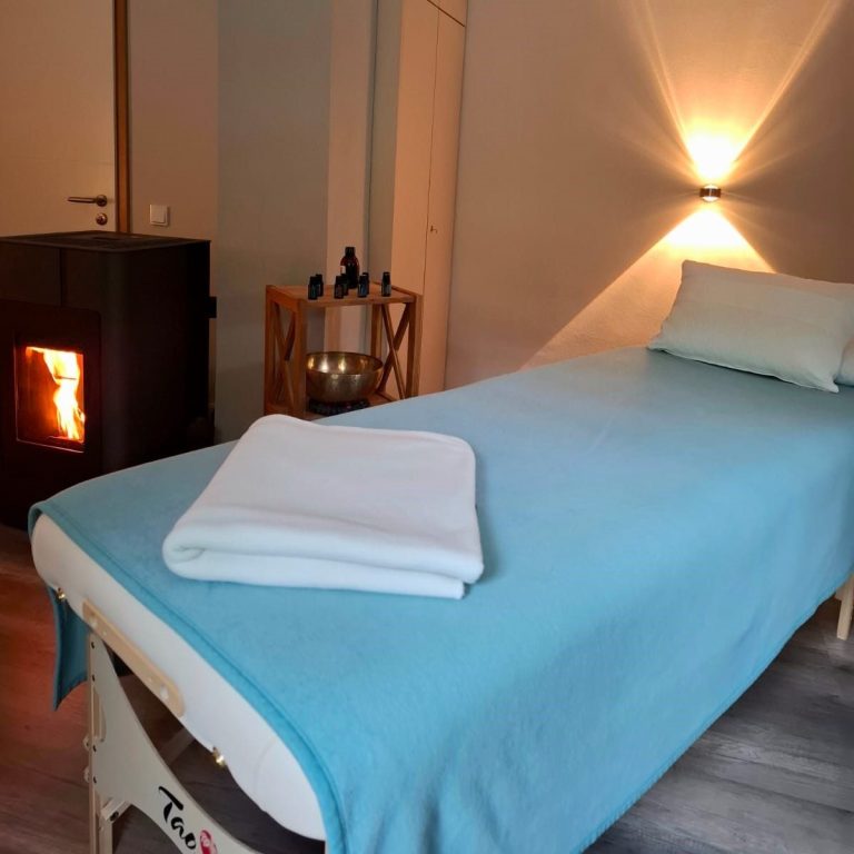 Wohlfühlraum mit Massagetisch, Klangschalen und einem Kamin.