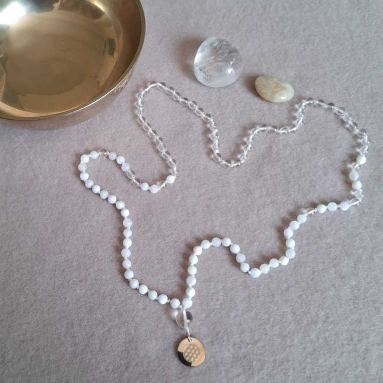 Perlenkette mit silbernem Anhänger, transparentem Kristall und Schale auf einem hellen Untergrund.