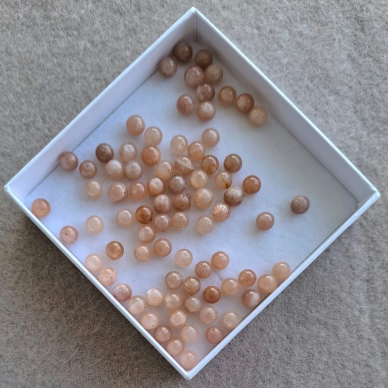 Mondstein Perlen rose Eine quadratische Schachtel mit vielen kleinen, rosa Perlen.