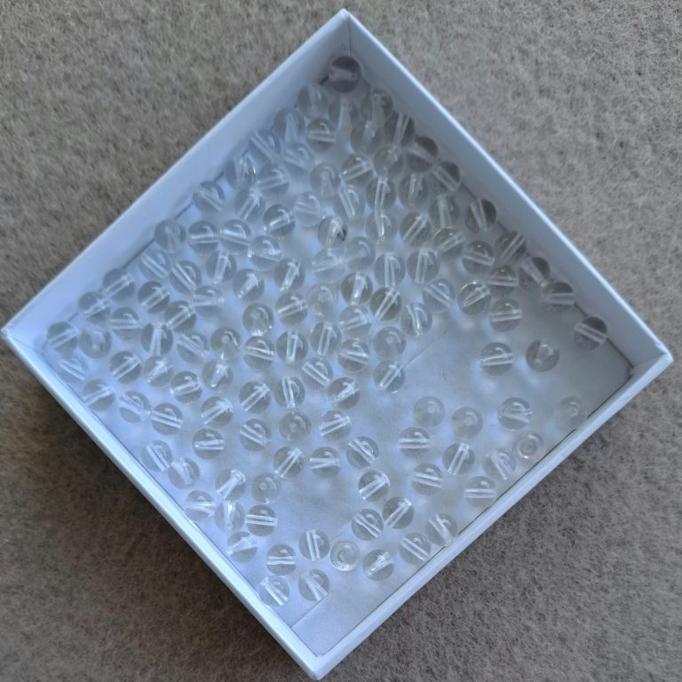 Bergkristall Perlen Eine weiße Schachtel mit vielen kleinen durchsichtigen Perlen.