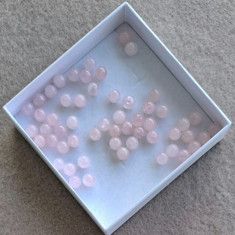 Rosenquarz Perlen Rosa Perlen in einer weißen Schachtel auf einem neutralen Untergrund.