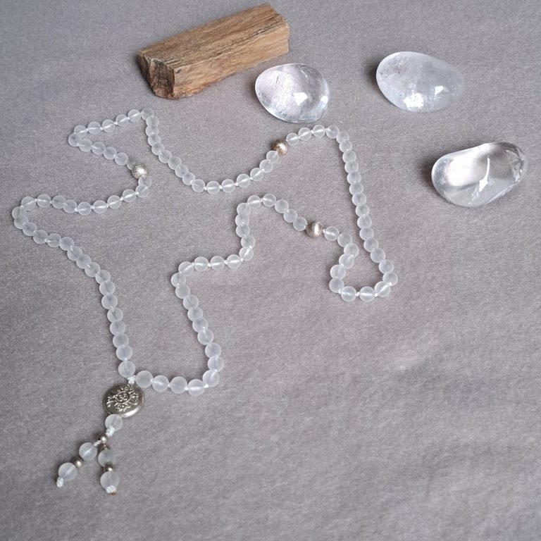 Perlenkette mit Anhänger, umgeben von klaren Steinen und einem Holzstück.