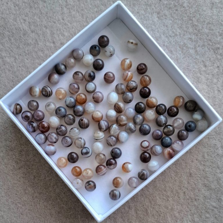 Botswana Achat Perlen Eine quadratische Schachtel mit vielen bunten, glänzenden Perlen.