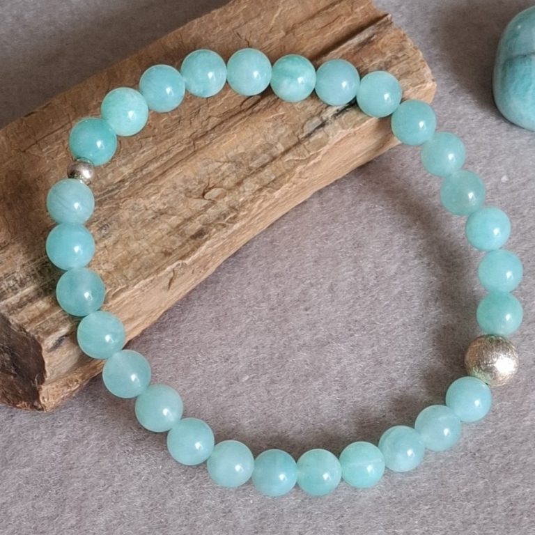 Türkise Perlenarmband auf braunem Holzstück mit zwei silbernen Perlen.