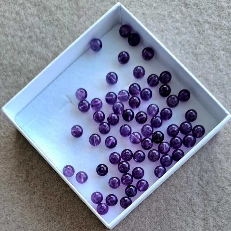 Amethyst Perlen Eine flache Schachtel mit vielen lila Perlen.