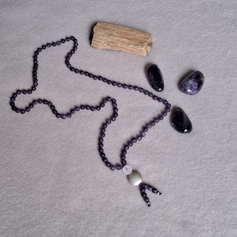 Lila Halskette aus Perlen mit einem silbernen Anhänger und drei lila Steinen.