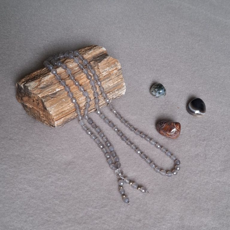 Kette mit grauen Steinen, neben zwei weiteren bunten Steinen auf einem Holzstück.