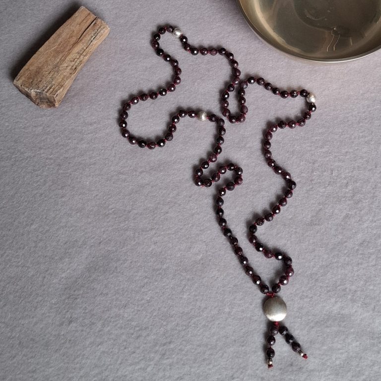 Rote Perlenkette mit Silberakzenten auf einem grauen Untergrund.