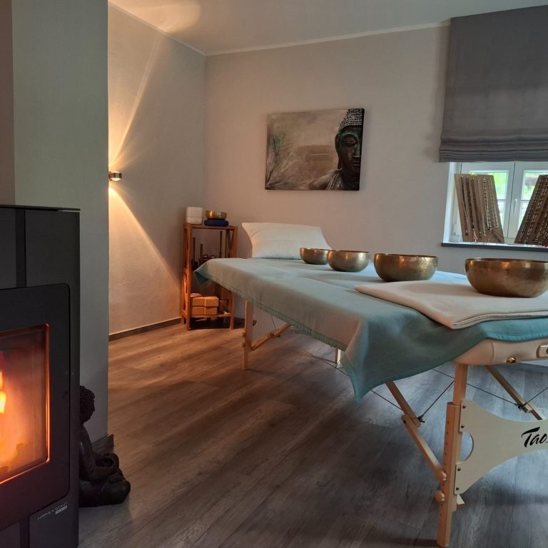 Ruhiger Wellnessraum mit Massagetisch, Klangschalen und Kamin.